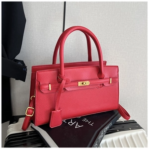 Close-up of red lychee pattern leather bag with golden twist lock on white suitcase