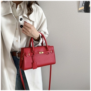 Détail du sac à main rouge en cuir grainé avec fermoir rotatif en métal et bandoulière fine