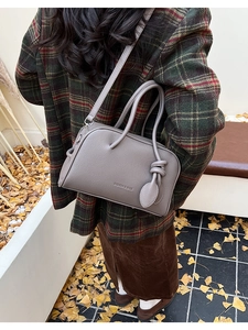 Photo en extérieur d'un sac à bandoulière gris texturé avec poignées et breloque nouée