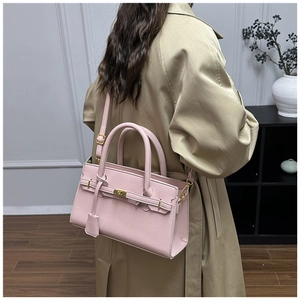 Detail of pink lychee leather bag with gold hardware worn over a khaki trench coat