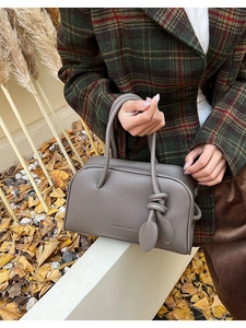 Détail du sac à main gris en cuir grainé avec un pendentif nœud et le logo de la marque