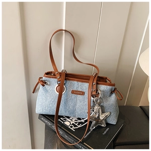 Close-up of denim shoulder bag with brown leather trim and star pendant detail