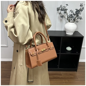 Détail de sac à main marron en cuir grainé avec fermoir rotatif et bandoulière sur manteau