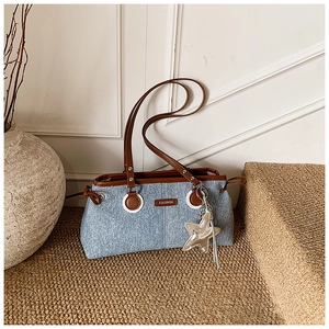 Detail of blue denim shoulder bag with brown leather trim and silver star charm