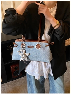 Detail of denim tote bag with brown leather trim and shiny silver star pendant