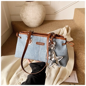 Close-up of denim shoulder bag with leather trim and star pendant detail