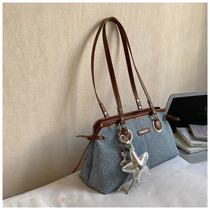 Detail of blue denim tote bag with brown leather handles and silver star charm accessory