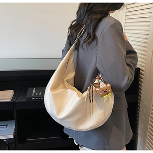 Detail van de beige hobo tas met beertjeshanger, gedragen als stijlvolle schoudertas