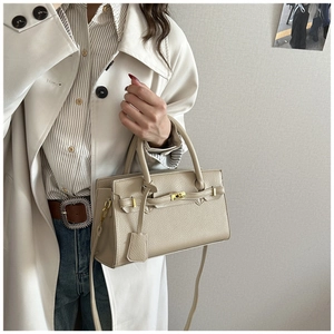 Détail d'un sac à main beige en cuir grainé avec fermoir doré et poignée supérieure