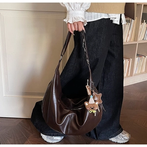 Detailweergave van een grote bruine hobo-tas met een berenbedeltje in een knusse kamer