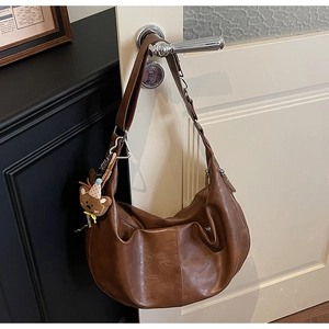 Detail van een bruine hobo-tas met geplooide textuur en een beer pluche hanger