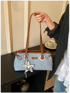Detail of denim shoulder bag featuring brown leather trim and metallic star charm