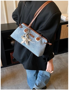 Close-up of denim tote bag with brown leather trim and shiny silver starfish pendant
