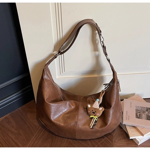 Bruine hobo crossbody tas met berenhanger getoond in een sfeervolle binnensetting