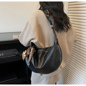 Detail van zwarte hobo schoudertas met zilveren hardware en een bruine berenhanger