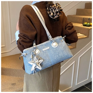 Detail of blue denim shoulder bag with silver star charm and metallic logo plate