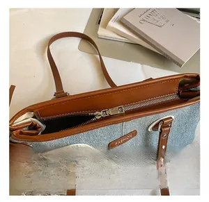 Detalle del bolso tote de mezclilla azul con asas de cuero marrón, cremallera y estrella