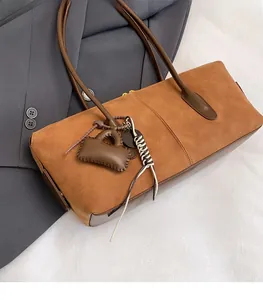 Detailed side view of brown suede tote bag with slim shoulder straps and matching charm