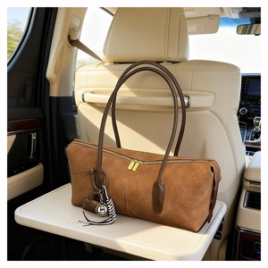 Close-up of brown suede handbag featuring a 100 charm and gold zipper on car table