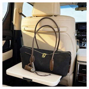 Macro detail of black matte shoulder bag with gold zipper and brown leather charm