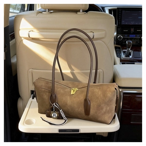 Detail of vintage brown suede shoulder bag with gold zipper and striped pendant in a car