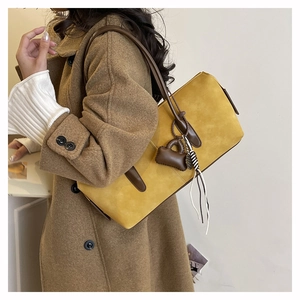 Detail of yellow matte faux leather shoulder bag with brown straps and heart charm