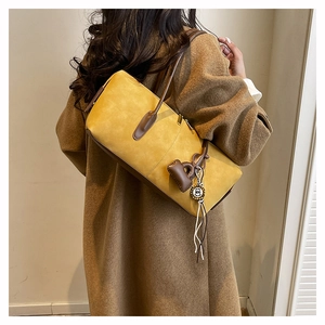 Detail view of mustard yellow suede tote bag with brown leather handles and heart charm