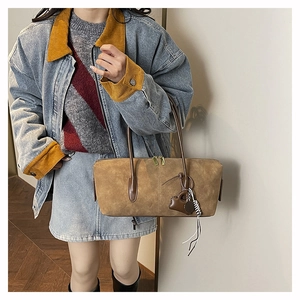 Close-up of brown suede hobo bag with heart charm and fringe on a model's shoulder