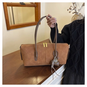 Close-up of brown suede shoulder bag with dual gold zippers and a bear charm on wood