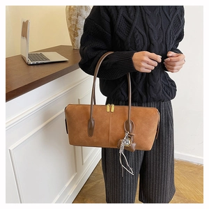 Close-up of brown suede shoulder bag featuring dual gold zippers and decorative charm