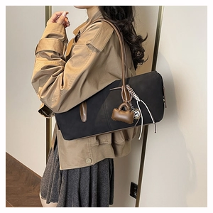 Detail of a black rectangular tote bag with brown leather straps and decorative charms
