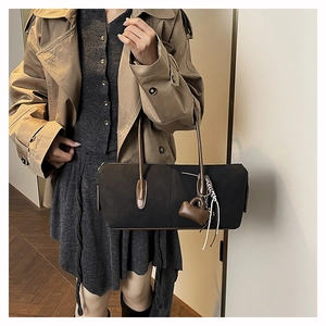 Detail view of black rectangular Boston bag with brown leather handles and fringe charm