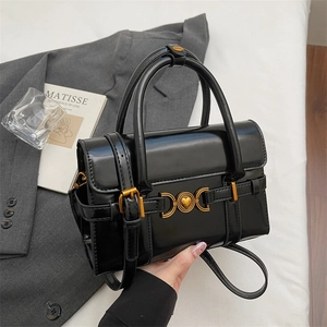 Sac à main noir brillant avec cœur doré posé sur une parure de lit blanche