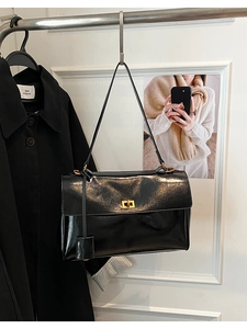 Macro detail of glossy black leather shoulder bag featuring a gold rectangular twist lock