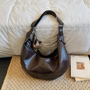 Donkerbruine leren hobo-tas met beer-bedel tegen een warme lifestyle-achtergrond