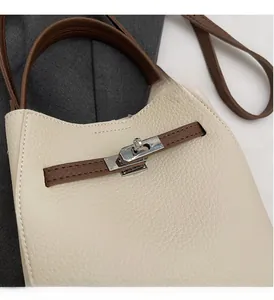 Détail du fermoir rotatif argenté et du cuir grainé crème sur un sac composite
