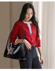 Détail d'un grand sac cabas en cuir noir avec deux poches avant et un gland orange vif