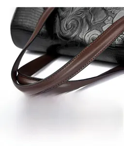 Dettaglio borsa nera con goffratura floreale e manico in pelle liscia marrone scuro