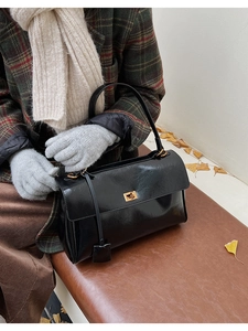 Detail of black glossy shoulder bag with gold hardware on a vintage leather bench