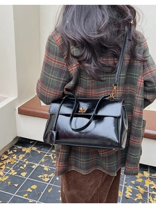 Close-up of black glossy leather bag with golden twist lock on a vintage plaid coat