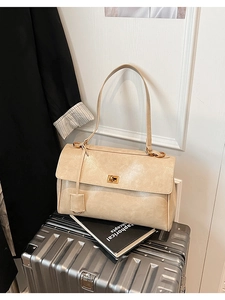 Close-up of beige leather shoulder bag with golden clasp resting on a silver suitcase