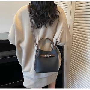 Détail du sac seau en cuir grainé noir avec poignée marron et fermoir rotatif argenté