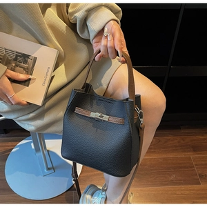 Détail du sac seau en cuir grainé noir avec lanières brunes et fermoir rotatif en métal argent