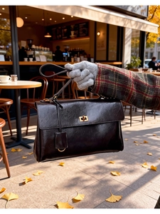 Detail of vintage textured leather handbag with metal turn-lock and ginkgo leaf backdrop