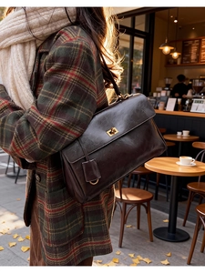 Detail of vintage coffee messenger bag with gold twist lock on a plaid wool coat