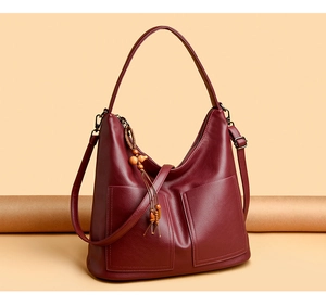 Détail du sac bandoulière en cuir bordeaux avec pompon en perles de bois et poches