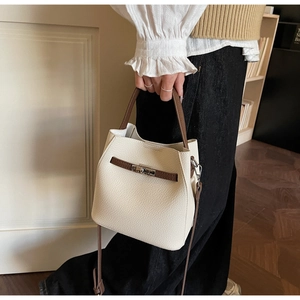 Détail du sac seau crème avec lanières marron et fermoir argenté porté par un modèle