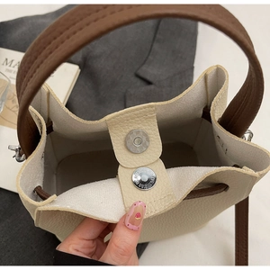 Gros plan d'un sac seau en cuir beige avec boucles magnétiques argentées et texture grainée