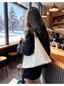 Minimalist white leather tote bag shown on model in a snowy cafe setting