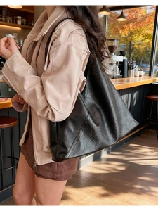 Large black leather tote bag shown on a model in a cozy cafe setting during autumn